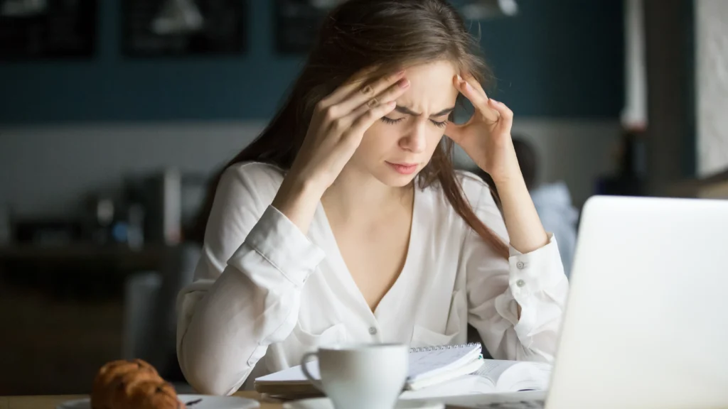 A woman experiencing stress or frustration at a desk, highlighting the role of emotional factors in what causes acne