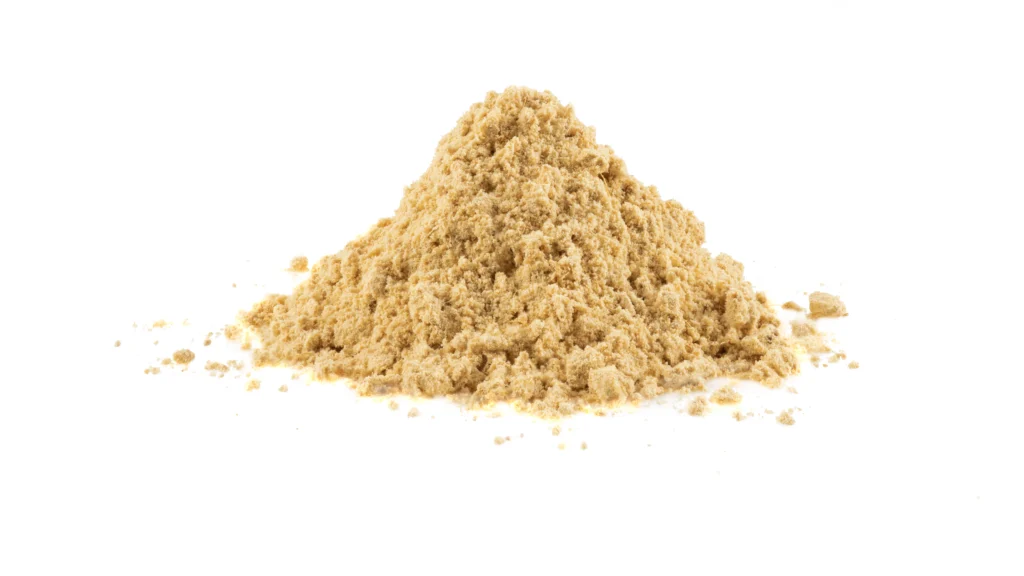 A mound of yellowish-golden nutritional yeast flakes sits against a stark white background, showcasing its flaky, powdery texture.
