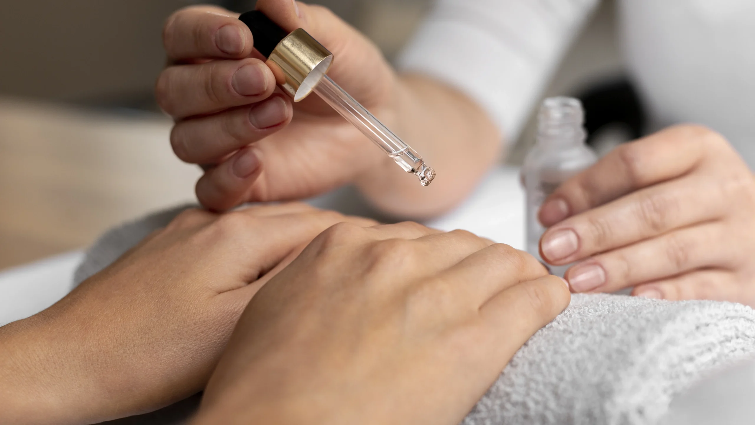 A close-up of a hand holding a dropper bottle filled with clear liquid, carefully applying it to another person's arm, demonstrating an essential step in how to remove gel nail polish safely and effectively.