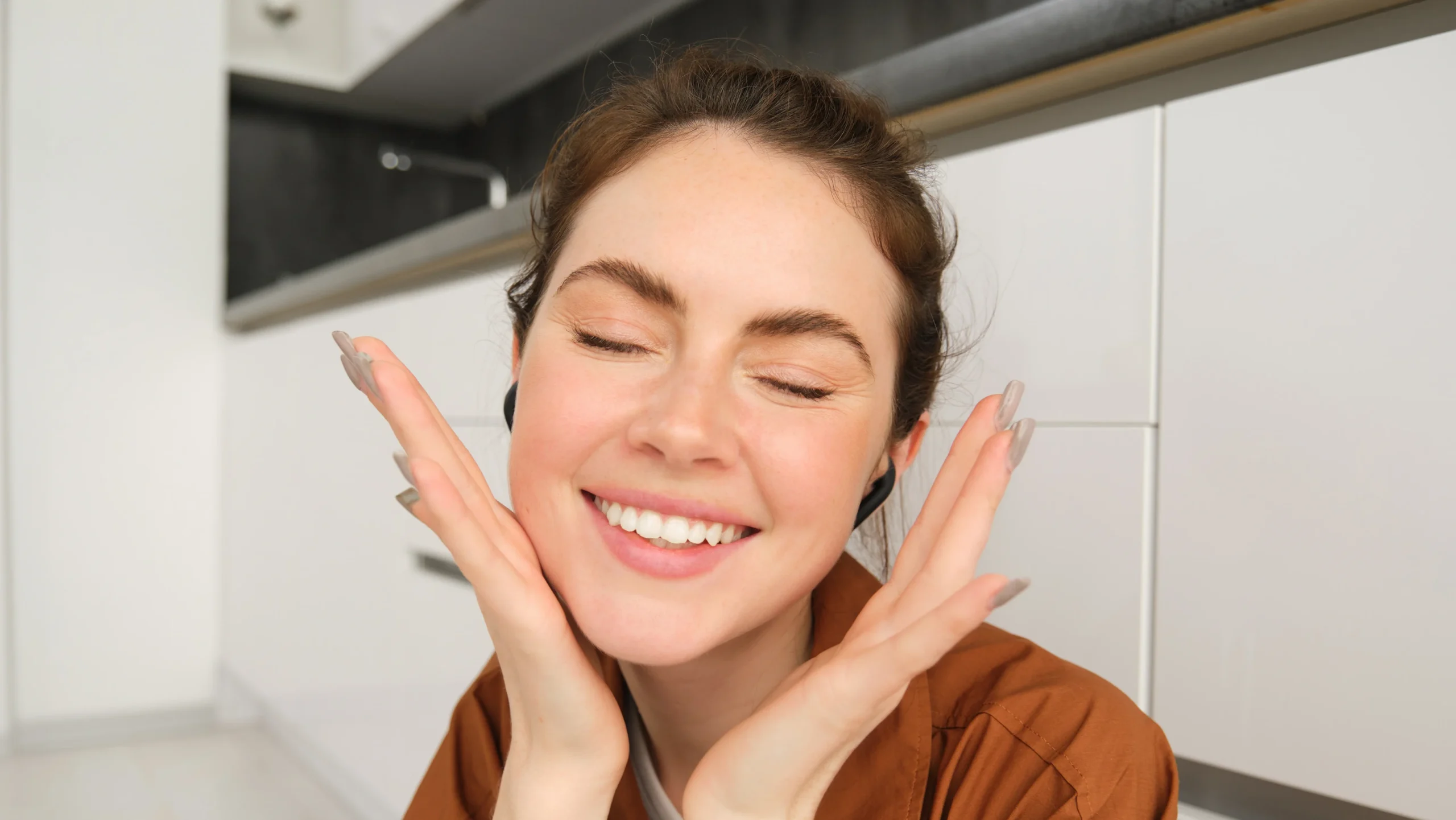 A woman with a bright smile and closed eyes gently touches her face, reflecting the potential skin health benefits of foods like yellow dragon fruit.