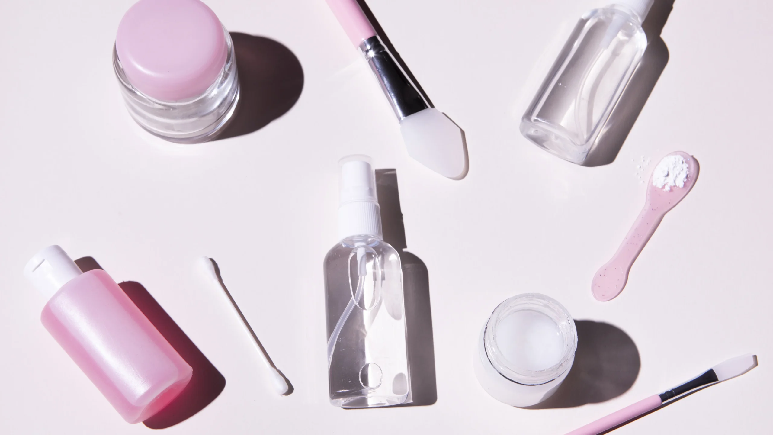 A collection of essential tools for how to remove acrylic nails including a small bottle with a pink cap, a clear brush applicator, and various nail care products arranged neatly on a clean surface